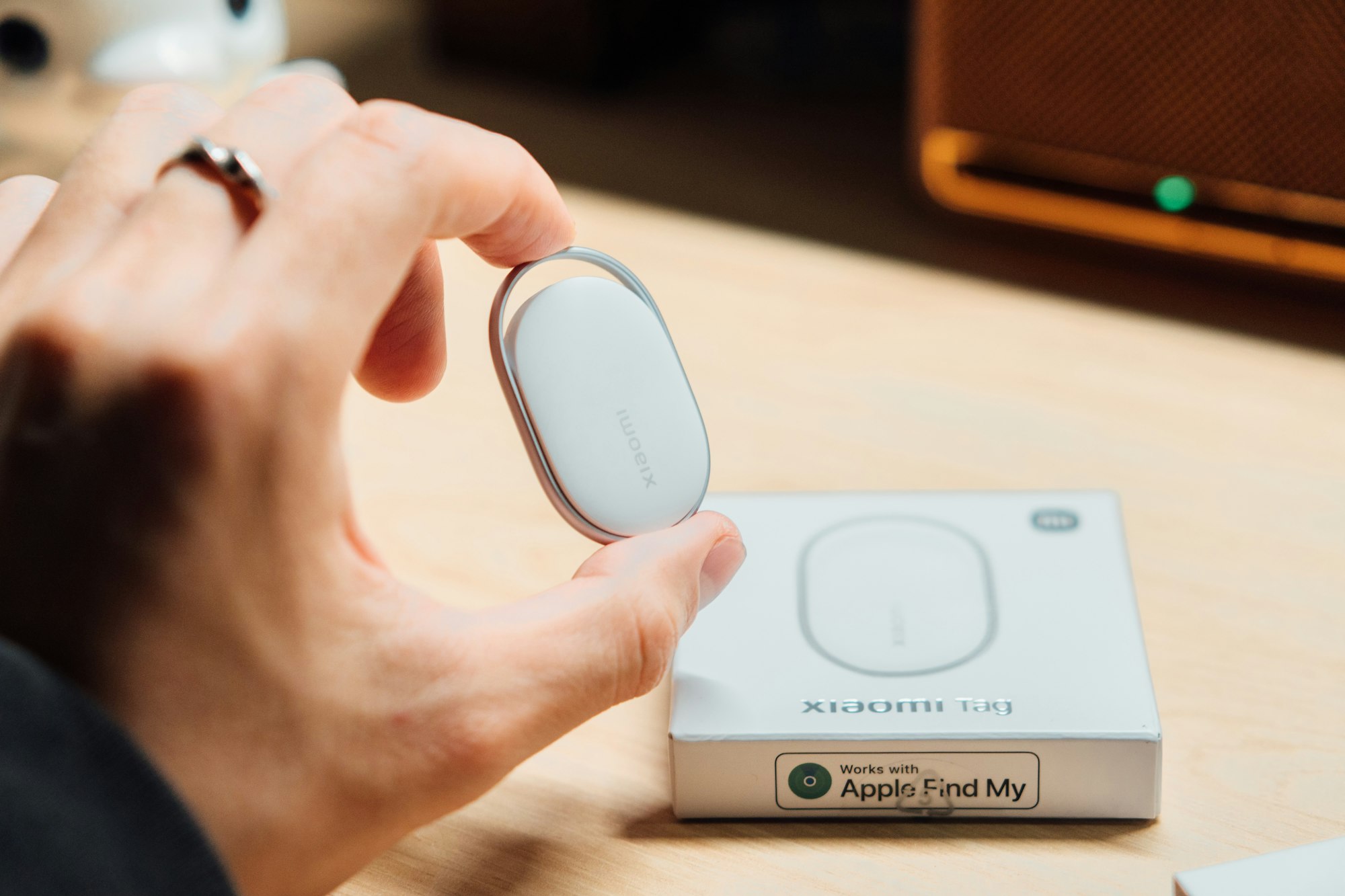 Hand holding a small Bluetooth item tracker next to its packaging box